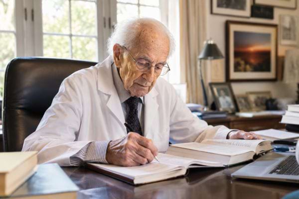 Médecin centenaire écrivant dans un carnet, entouré de livres, pour garder l’esprit en éveil.