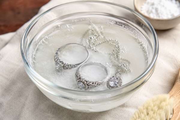 Vintage silver rings and a delicate silver necklace soaking in a small glass bowl filled with water