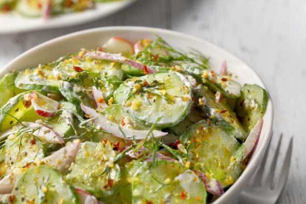 une salade de concombre en tranches avec une sauce dans une assiette blanche