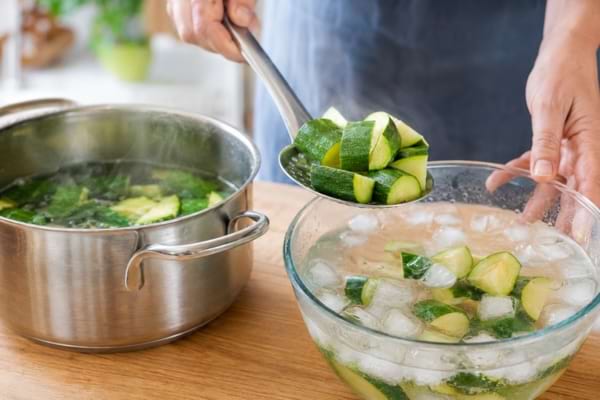 Morceaux de courgettes blanchis transférés dans un saladier rempli d’eau glacée.