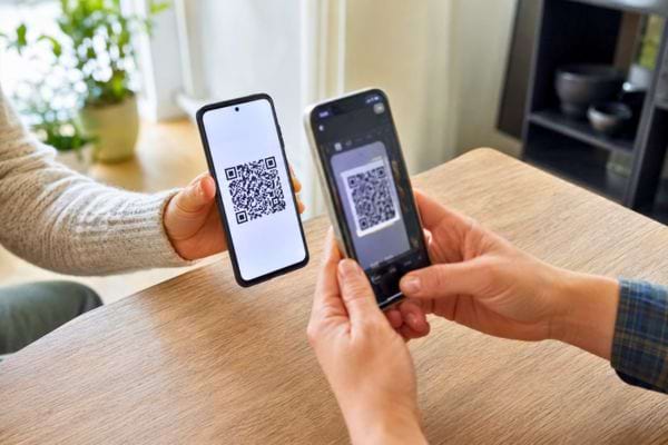 Un smartphone scanne le QR code Wi-Fi affiché sur un autre téléphone pour se connecter rapidement.