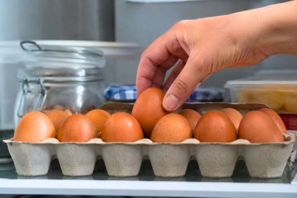 Main pla&ccedil;ant des &oelig;ufs dans leur bo&icirc;te sur une &eacute;tag&egrave;re du frigo