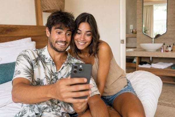 Couple en vacances regardant un selfie dans une chambre d’hôtel avec la salle de bains en arrière-plan.