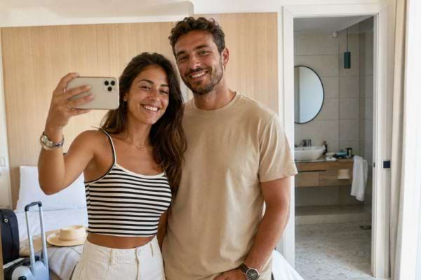 Jeune couple souriant prenant un selfie devant le miroir de sa chambre d’hôtel.