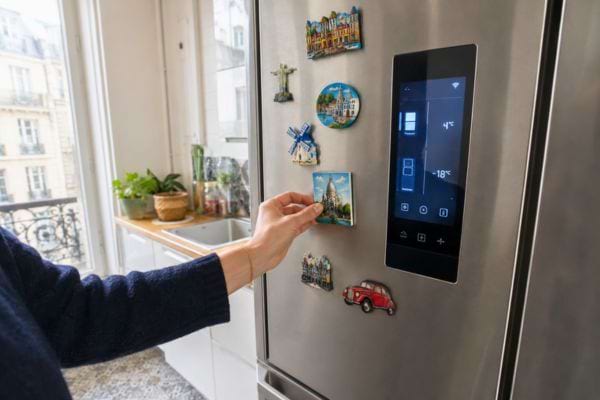 Main posant un magnet sur un frigo connecté en inox