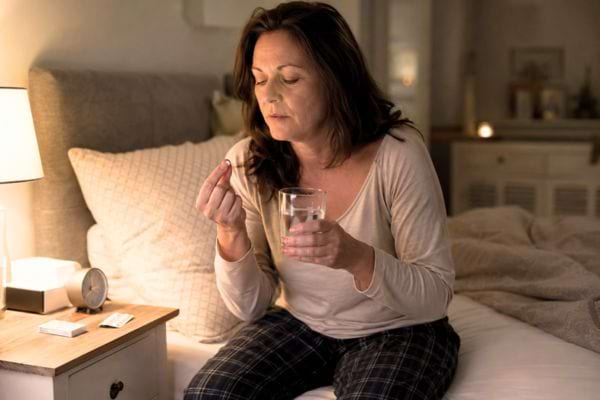 Femme prenant un somnifère au coucher, un usage pouvant favoriser des troubles de la mémoire.