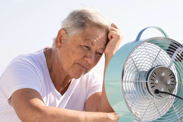 femme âgée devant un ventilateur bleu se tenant la tête