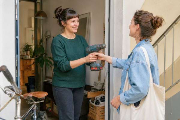 Deux voisines se prêtant une perceuse pour éviter un achat inutile et faire des économies.