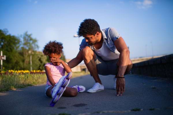 une petite fille afro pleure parce qu'elle est tombée en roller à côté d'un adulte qui la console
