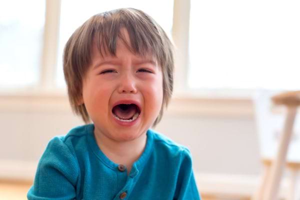 un petit enfant avec un pull bleu pleure