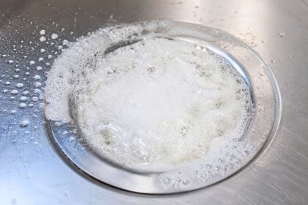 White powder and liquid vinegar reacting, bubbling and foaming intensely inside a clean stainless