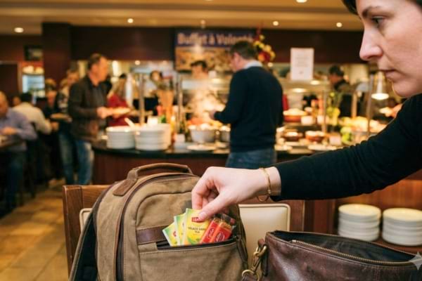 un client de restaurant glissant discrètement un petit objet dans son sac à dos posé sur une chaise