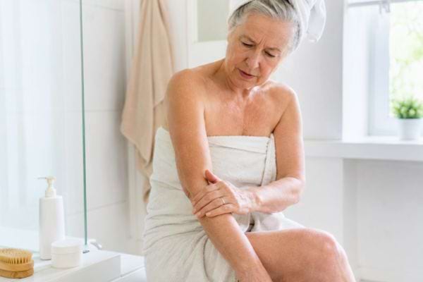 Femme de plus de 65 ans massant son bras apr&egrave;s la douche pour apaiser une peau s&egrave;che.