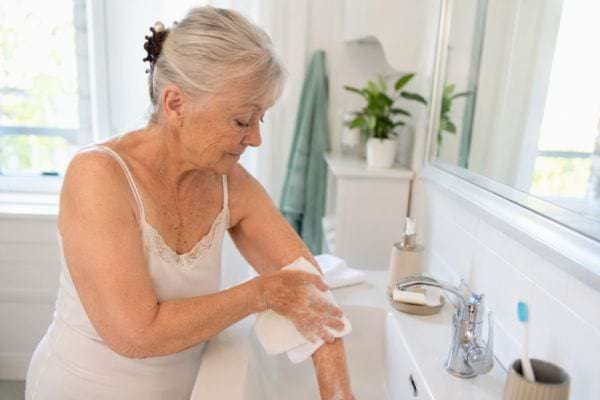 Femme &acirc;g&eacute;e se lavant les bras au lavabo entre deux douches pour pr&eacute;server sa peau.