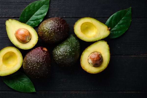 des avocats posés entiers et coupés en deux sur une table en bois