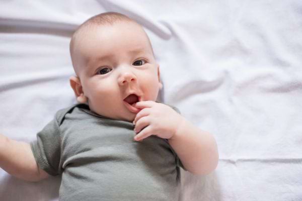 un bébé garçon sur le dos avec un body kaki sourit avec un doit dans la bouche