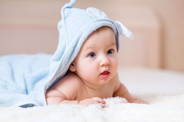 un bébé garçon sur le ventre avec une serviette bleu sur la tête