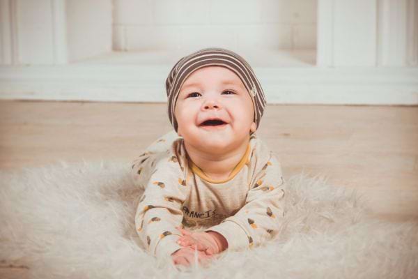 un bébé garçon sur le ventre sur un tapis avec un bonnet rayé sourit