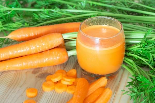 Jus de carotte frais entouré de carottes entières et coupées.