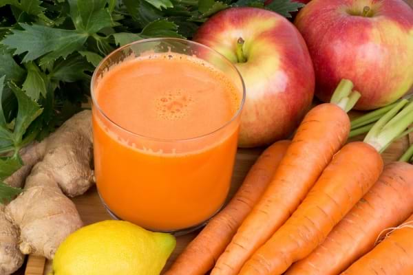 Jus de carotte, pomme, gingembre et citron entouré de ses ingrédients frais.
