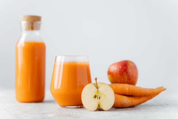 Jus maison à la pomme et à la carotte servi dans un verre et une bouteille.