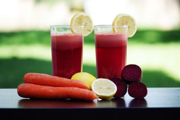 Deux verres de jus de betterave, carotte et citron préparés avec des légumes frais.