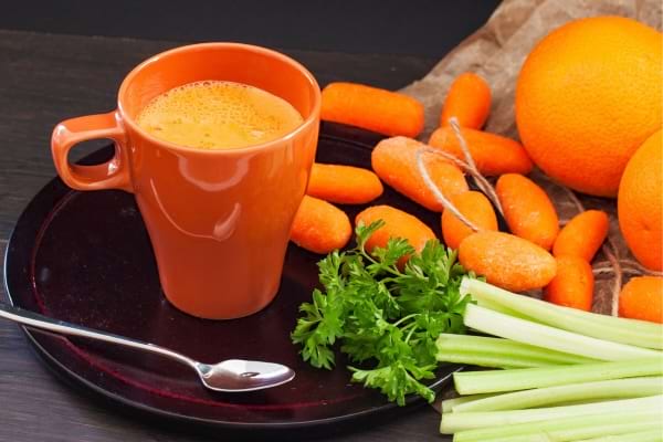 Jus de carotte, orange, céleri et persil servi dans une tasse orange.