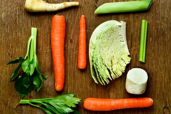 Carottes, chou, céleri, panais et poireau disposés sur une table en bois.
