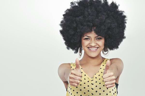 une jeune femme afro souriante les pouces en l'air et sûre d'elle