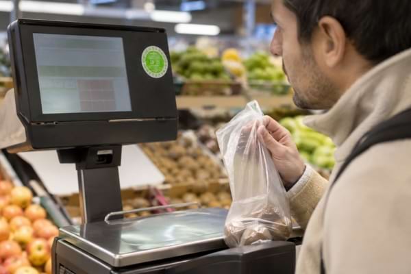 Client vérifiant la vignette verte de contrôle sur une balance de rayon frais.