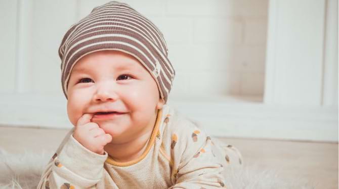 un b&eacute;b&eacute; gar&ccedil;on avec un doigt dans la bouche et un bonnet ray&eacute; blanc marron