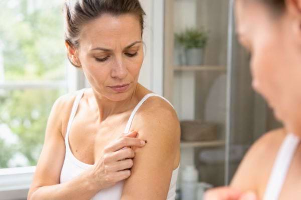 Femme examinant une petite lésion cutanée sur son épaule.