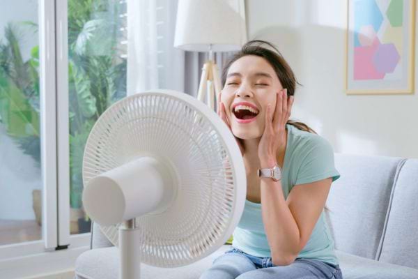 Femme jeune se rafraîchissant devant un ventilateur pendant une forte chaleur.