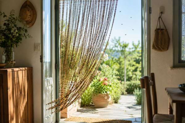 Rideau de perles extérieur devant une porte ouverte, avec insectes et jardin en été