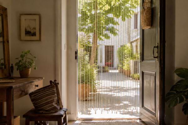 Rideau de perles sur une porte d’entrée extérieure, devant une cour ensoleillée
