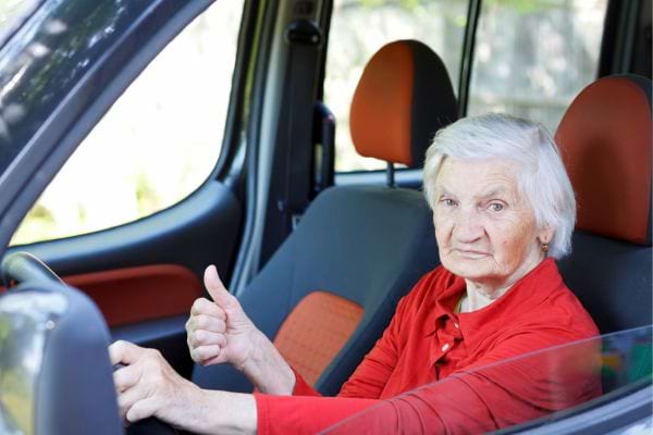 une vieille femme au volant d'une voiture fait un signe de la main avec son pouce levé