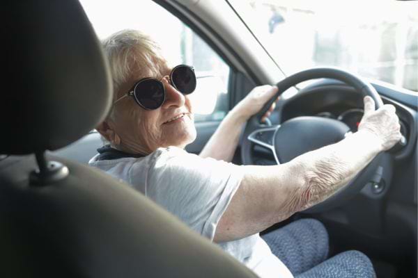 une femme âgée conduit une voiture avec des lunettes de soleil