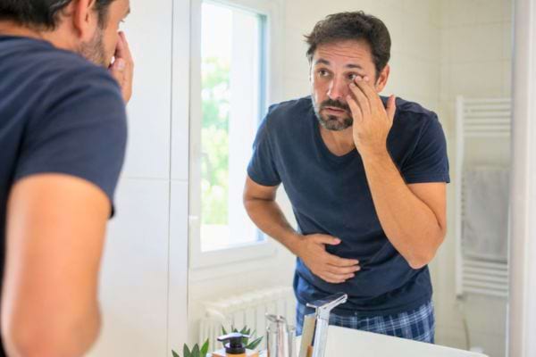 Homme fatigué devant le miroir avec douleur au ventre et yeux irrités