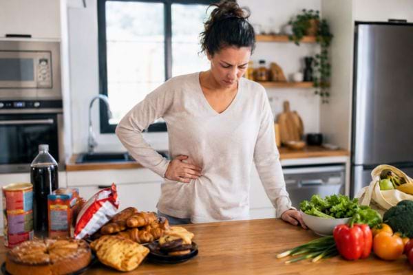 Femme ayant mal au ventre face à des aliments gras et des légumes