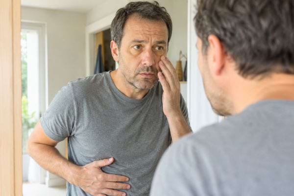 Homme observant son visage dans le miroir, fatigué et gêné au ventre, signes possibles d’un trouble du foie.