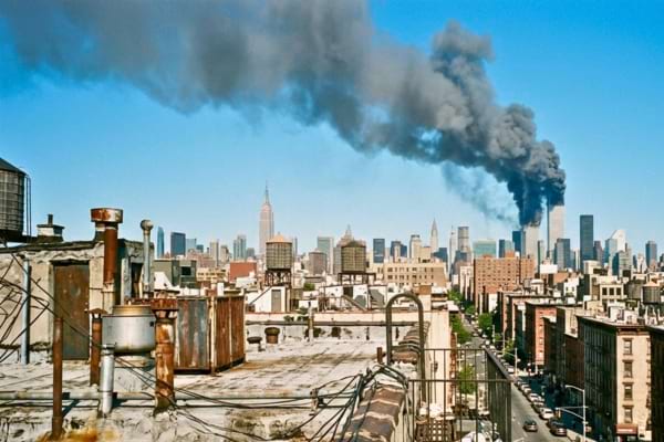 d'épaisses colonnes de fumée grise s'élèvent dans un ciel bleu clair, au-dessus de la silhouette des gratte-ciel.