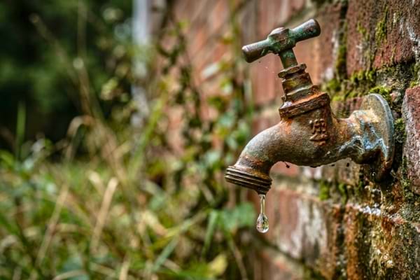 un robinet extérieur rouillé d'où tombe une seule goutte d'eau