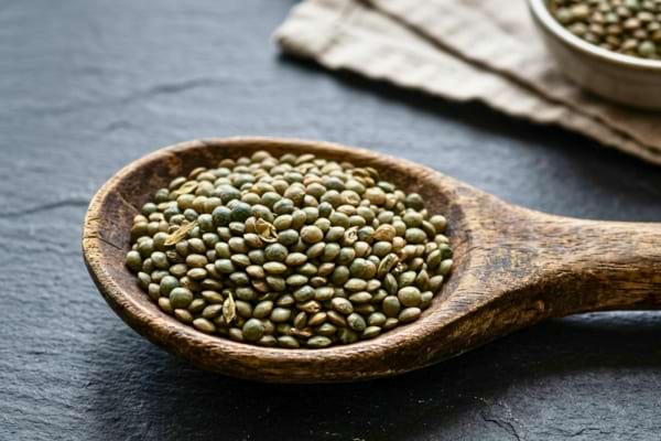 Un monticule de lentilles vertes crues dans une grande cuillère en boi