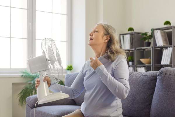 Femme âgée se rafraîchissant devant un ventilateur blanc pendant une forte chaleur.