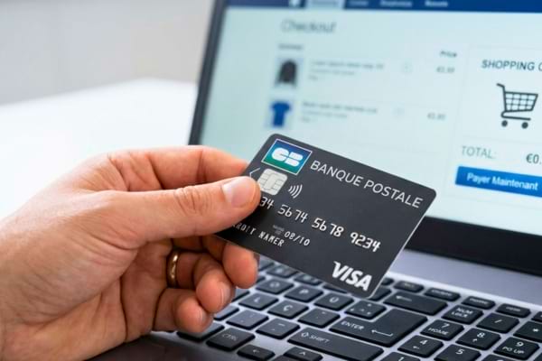 main tenant une carte bancaire près d'un clavier d'ordinateur, avec un écran flou