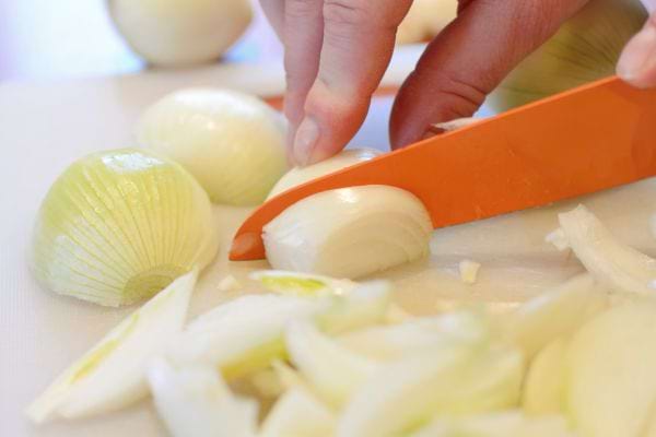 cuisinier qui coupe des oignons avec un gros couteau orange