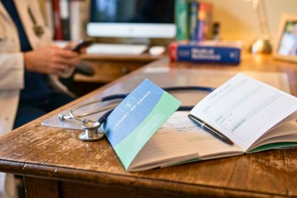 un stéthoscope et un carnet de santé pédiatrique posés sur une table en bois.