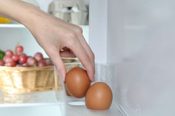 une femme prend un oeuf dur posé sur un range-oeuf dans la porte du frigo