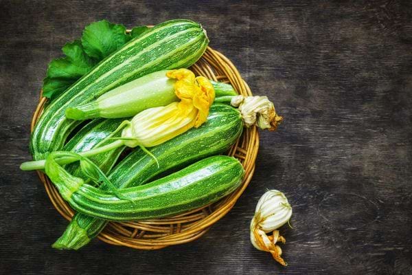 Panier rempli de courgettes fraîchement récoltées avec leurs fleurs.