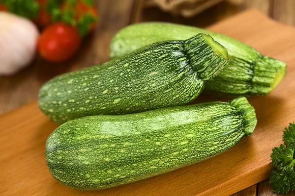 Trois courgettes fraîches posées sur une planche à découper en bois.